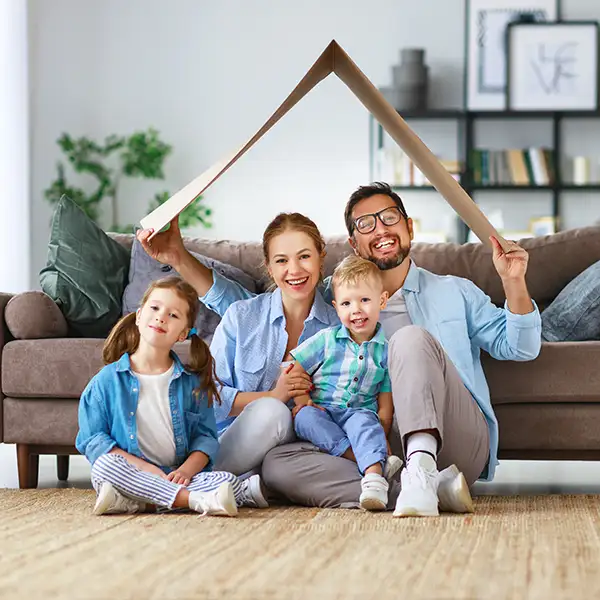 Family of four sitting in front of couch holding cardboard above heads 