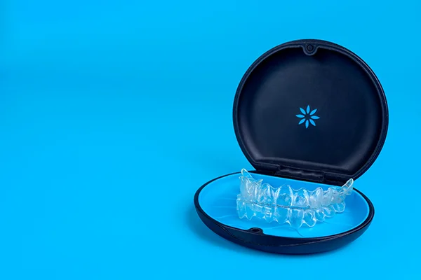 Set of clear aligners resting in an Invisalign® branded case on a blue background